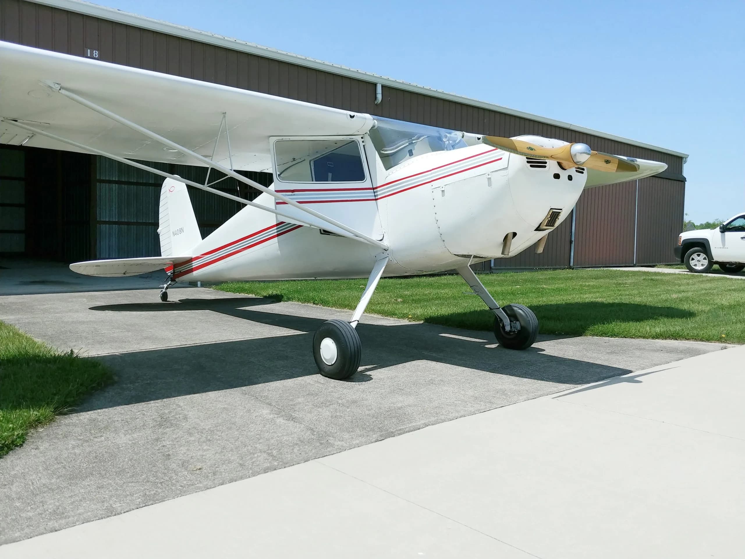 A white and red painted aircraft is parked on the tarmac in front of a hangar.