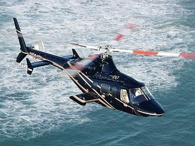 A sleek black helicopter with white stripes and red-tipped rotor blades flies over blue water.