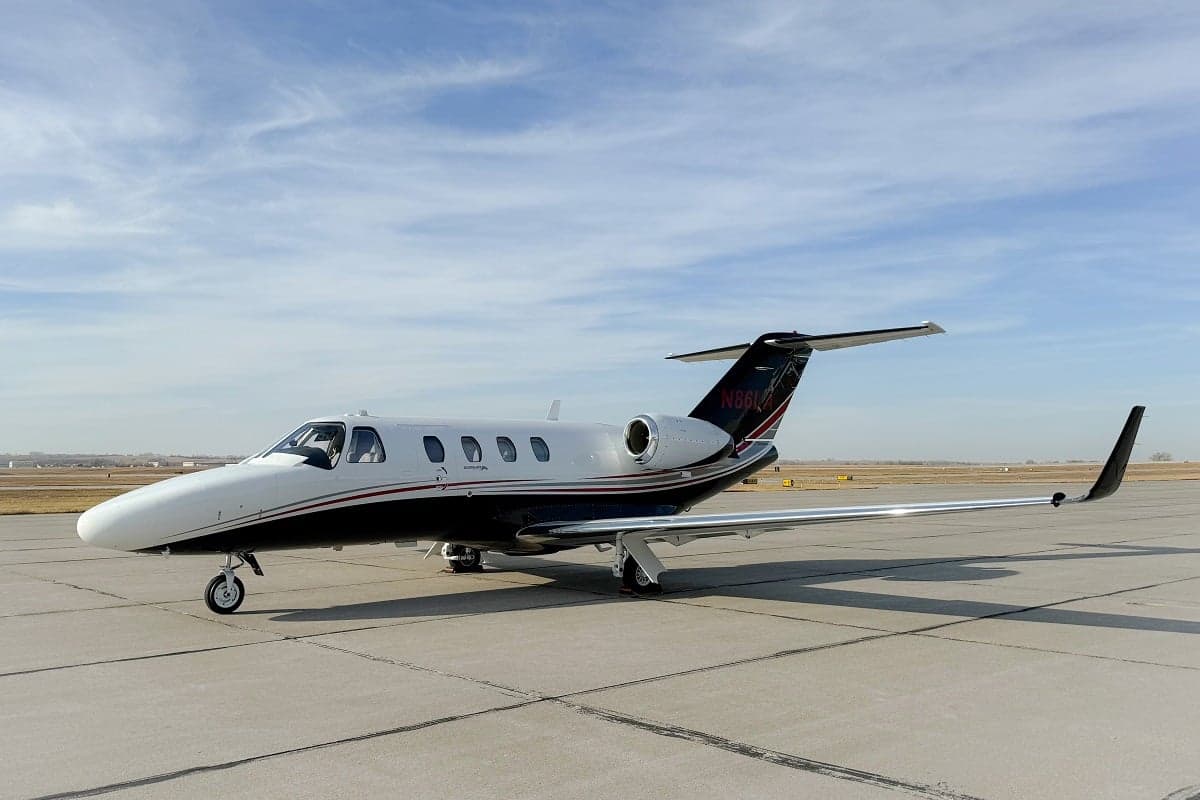 A Cessna Citation CJ3+ aircraft with a white and black paint scheme is parked on the tarmac.