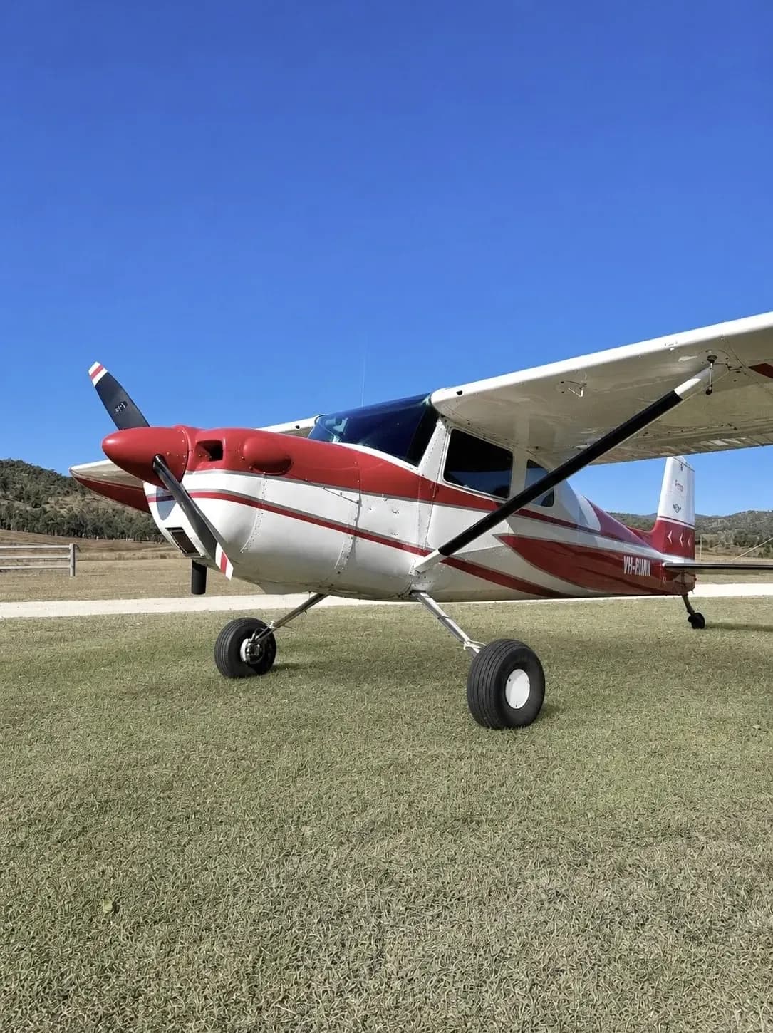 A red and white single-engine propeller aircraft with registration VH-RWM is parked on a grassy field under a clear blue sky.