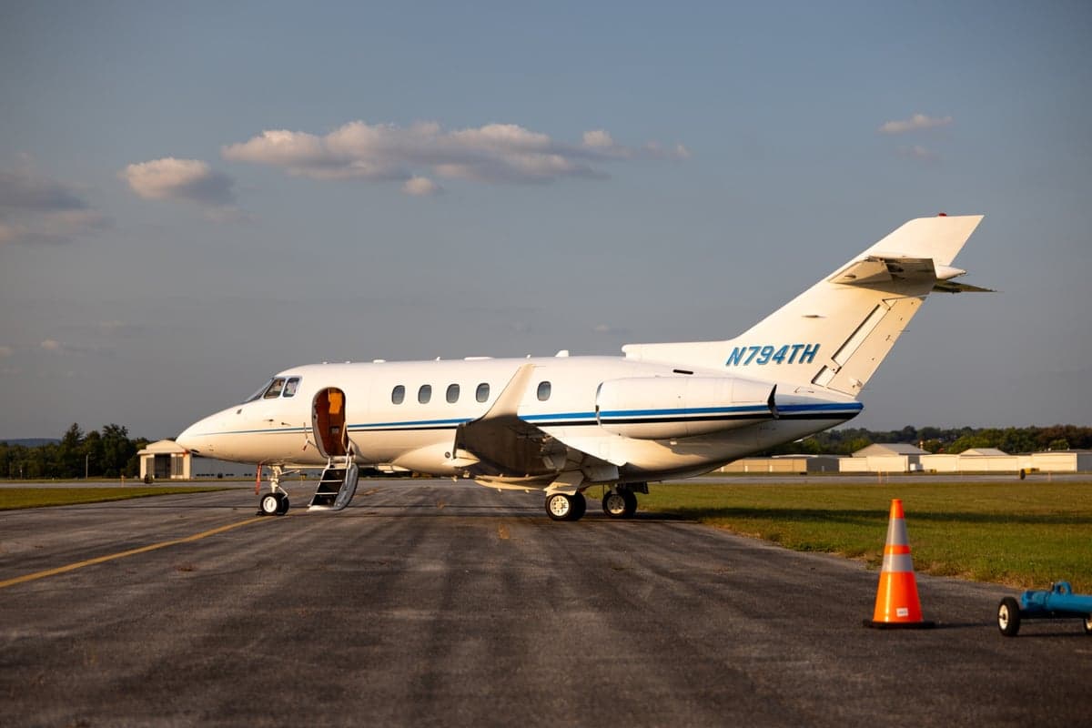 A white aircraft with blue stripes, registration N794TH, parked on the tarmac at dusk.