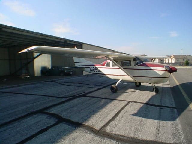 A white and red Cessna 206 aircraft (N1861Z) parked on an asphalt ramp next to a hangar.