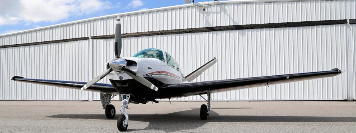 Front view of a Beechcraft Bonanza aircraft on the ground in front of a hangar.