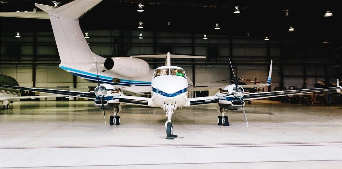 Front view of a twin turboprop aircraft in a hangar with a jet in the background.
