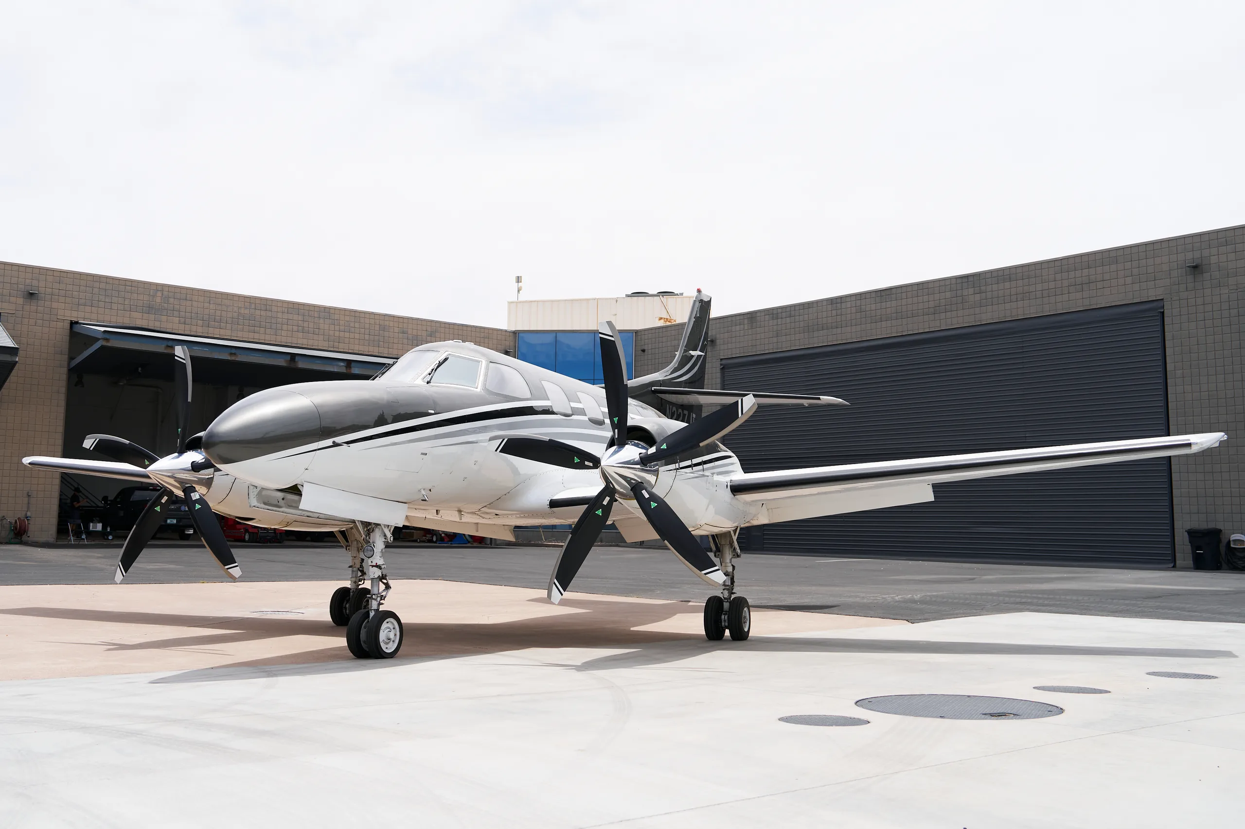 A white and black twin-engine turboprop aircraft, N227JT, parked on a tarmac in front of a hangar.