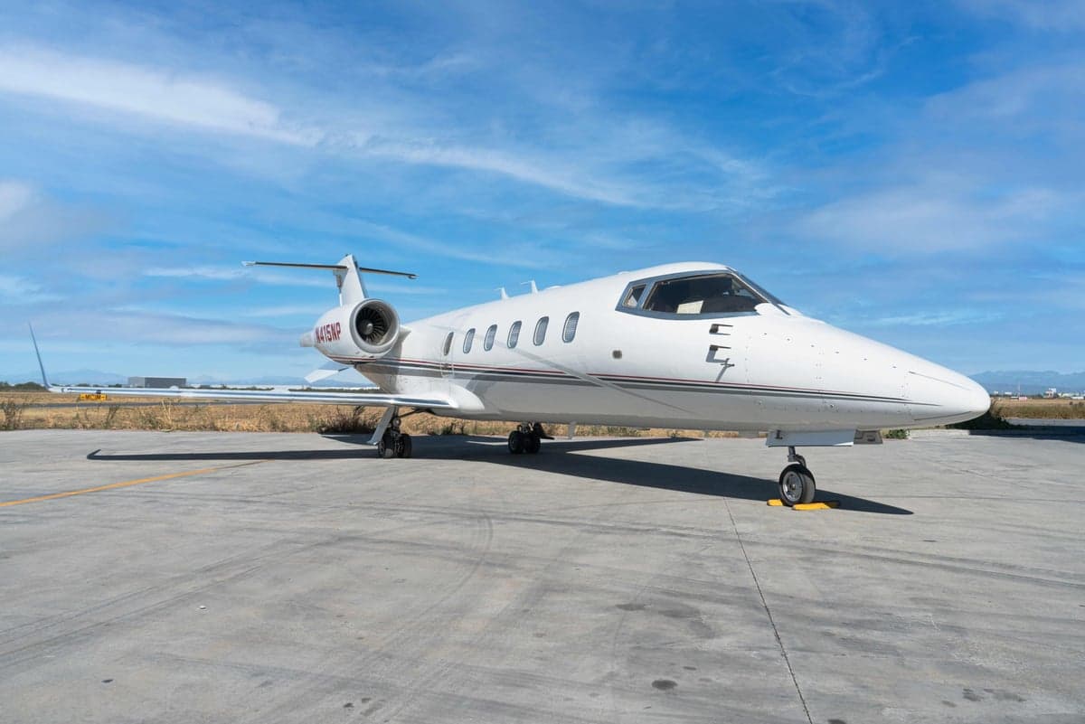 A white Learjet 45XR with registration N415NP is parked on the tarmac under a blue sky.