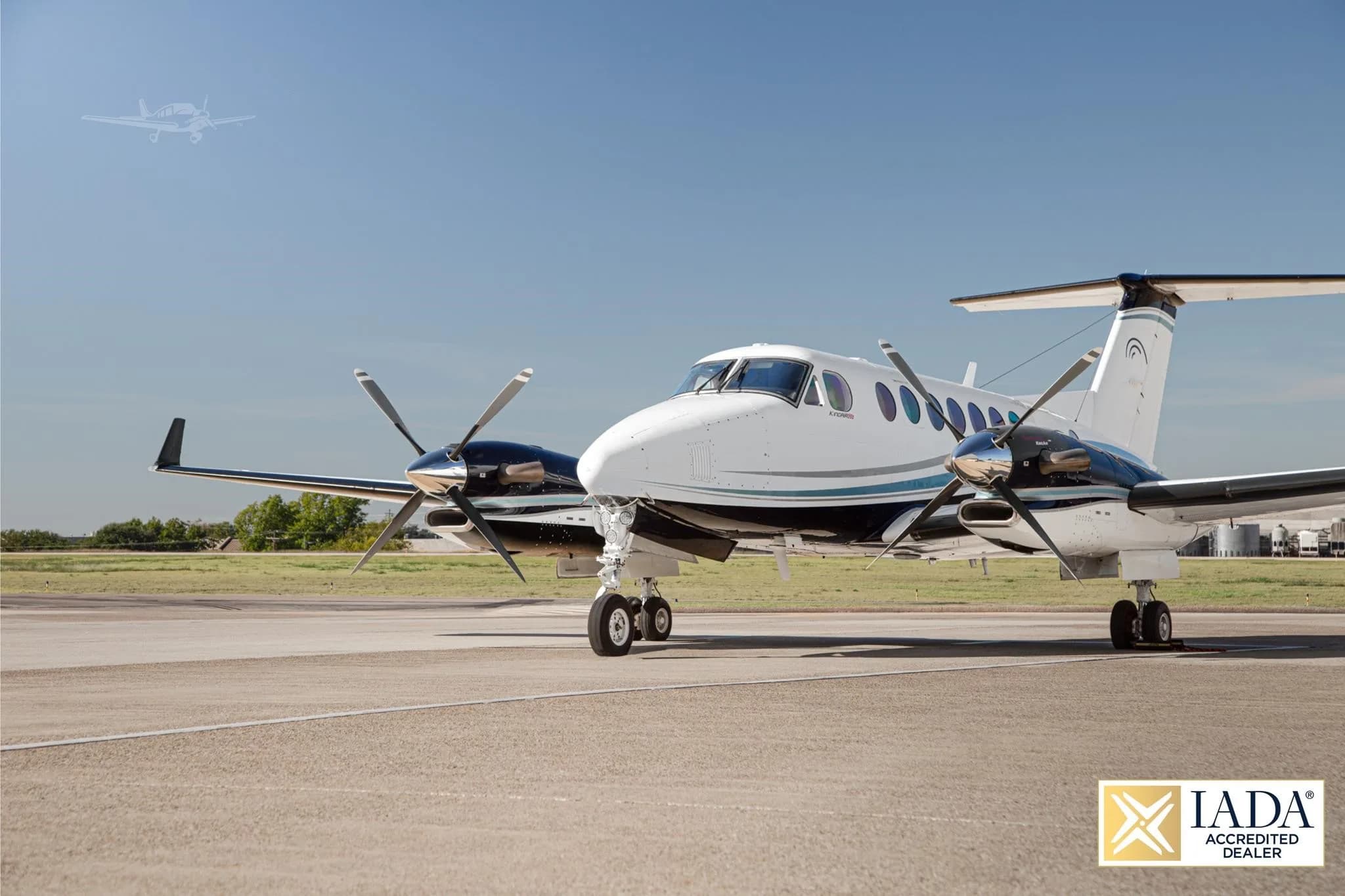 A white and black Beechcraft King Air twin-turboprop with a blue stripe, parked on a tarmac under a clear blue sky.