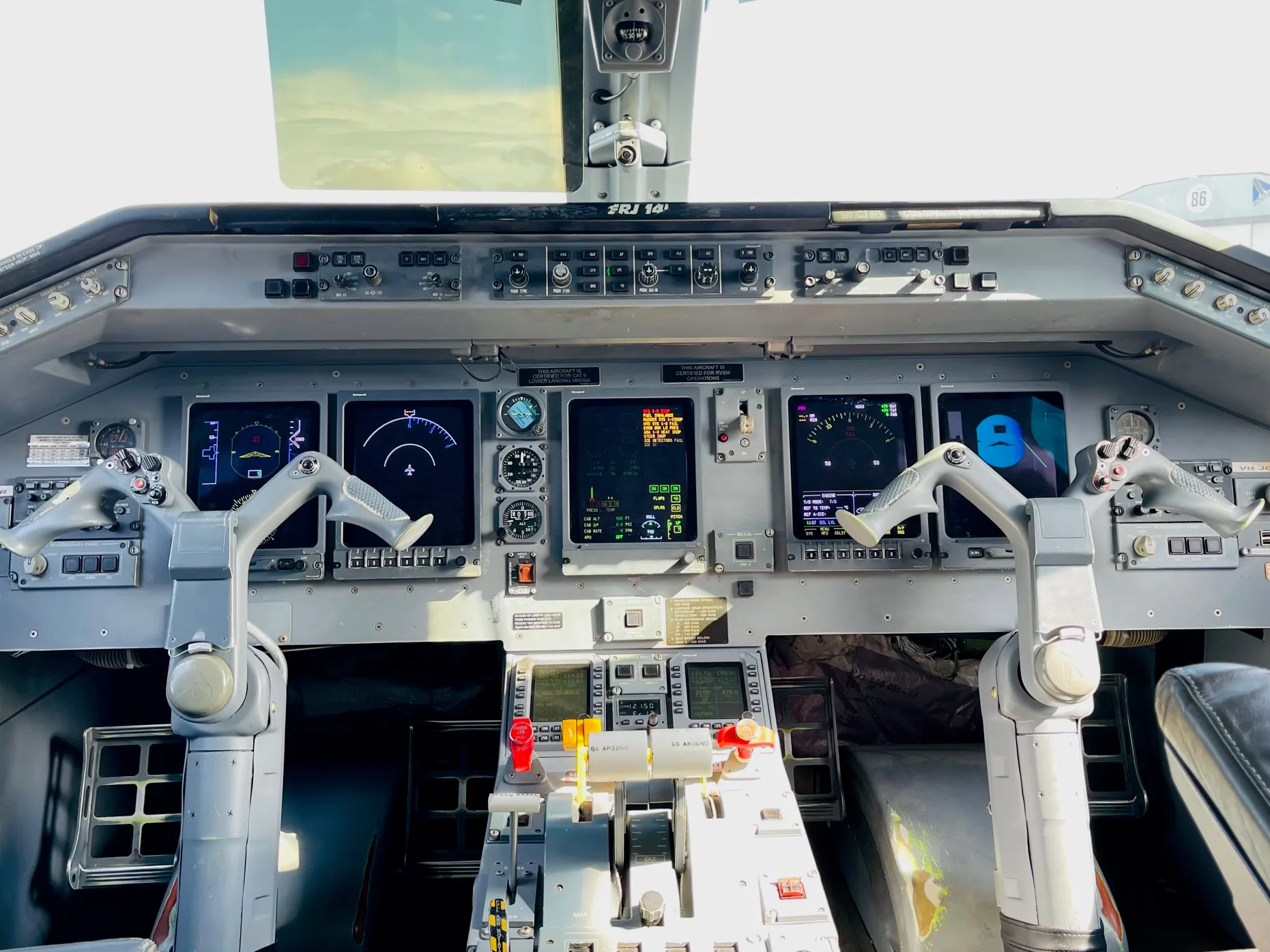 The cockpit of an Embraer ERJ 145 aircraft, showing the instrument panel, control yokes, and a view of the sky through the windshield.