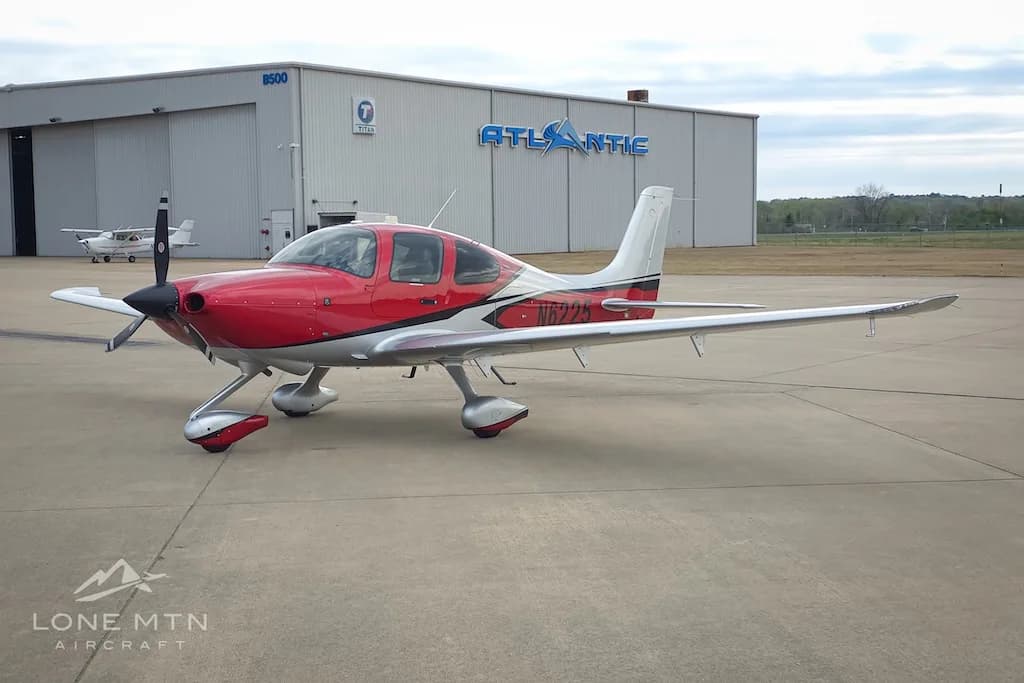 A red and silver Cirrus SR22 aircraft, N6225, parked on an airport apron in front of an Atlantic Aviation hangar.