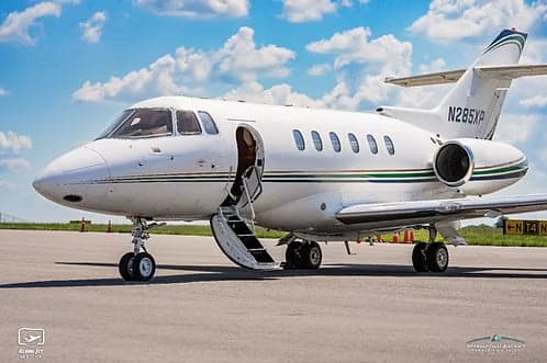 A white Hawker jet with tail number N285XP parked on the tarmac with the airstair door open.