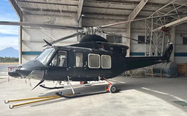 A black helicopter with skids parked inside a hangar, with mountains visible in the background.