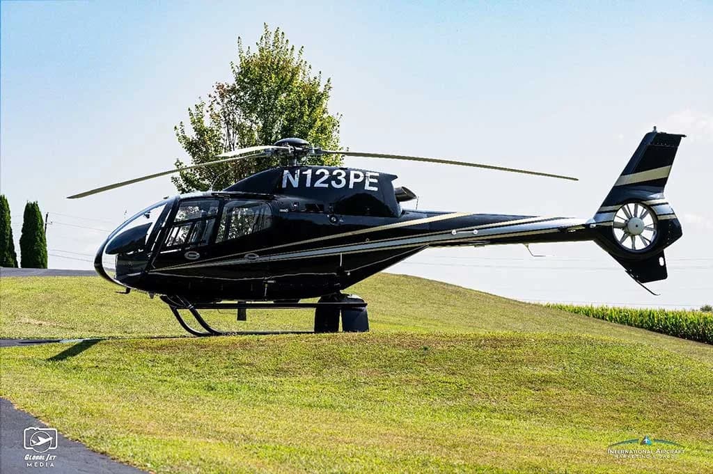 A black Eurocopter AS350 helicopter (N123PE) with silver stripes parked on a grassy hill.