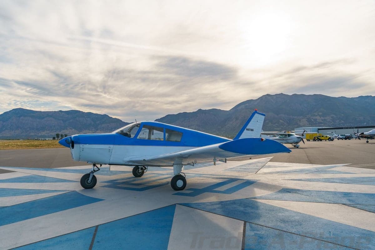 A blue and white single-engine aircraft, N8718N, parked on a blue and white patterned tarmac with mountains in the background.