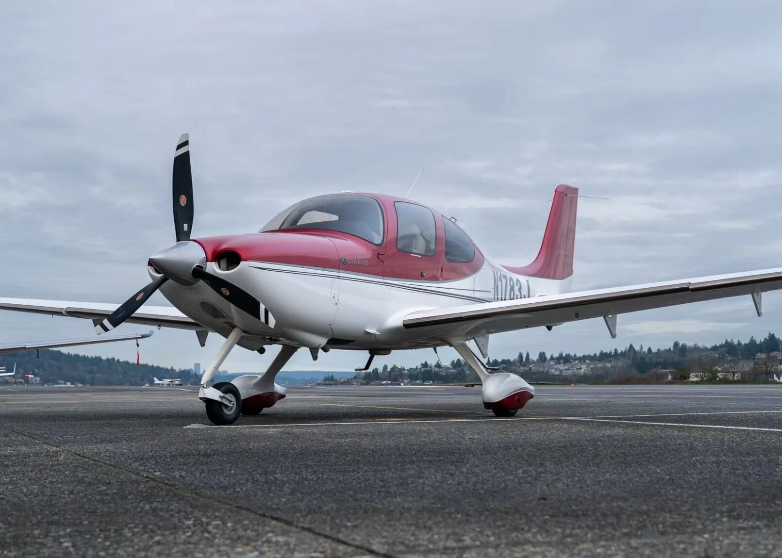 A red and white Cirrus SR22 aircraft, N1783J, parked on a tarmac under a cloudy sky.