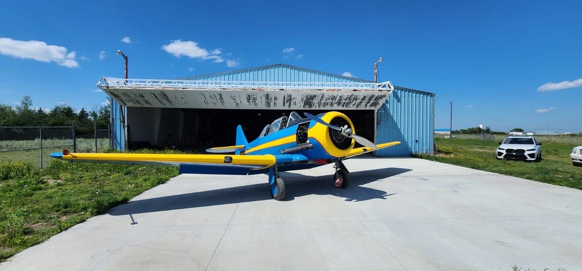 A blue and yellow aircraft is parked in front of an open hangar on a sunny day.