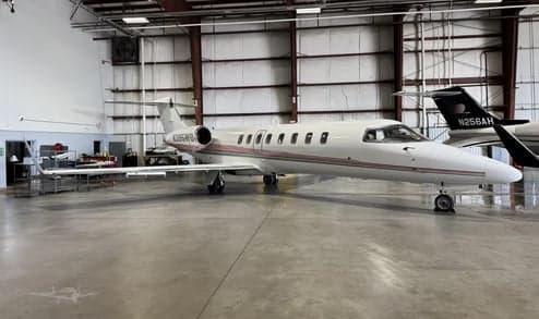 A white Learjet 35A business jet with red and grey stripes, registration N395WB, parked in a hangar.