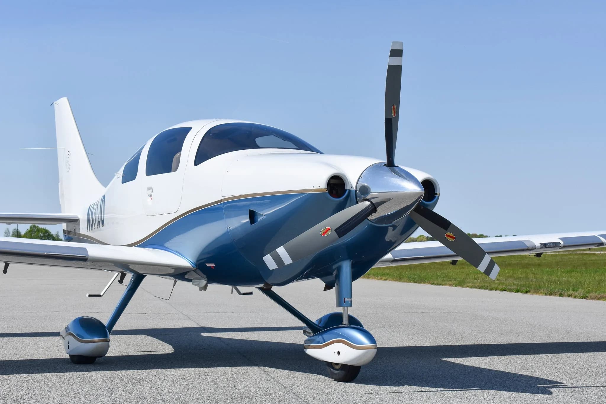 Front view of a white and blue single-engine aircraft with a propeller on an airfield.