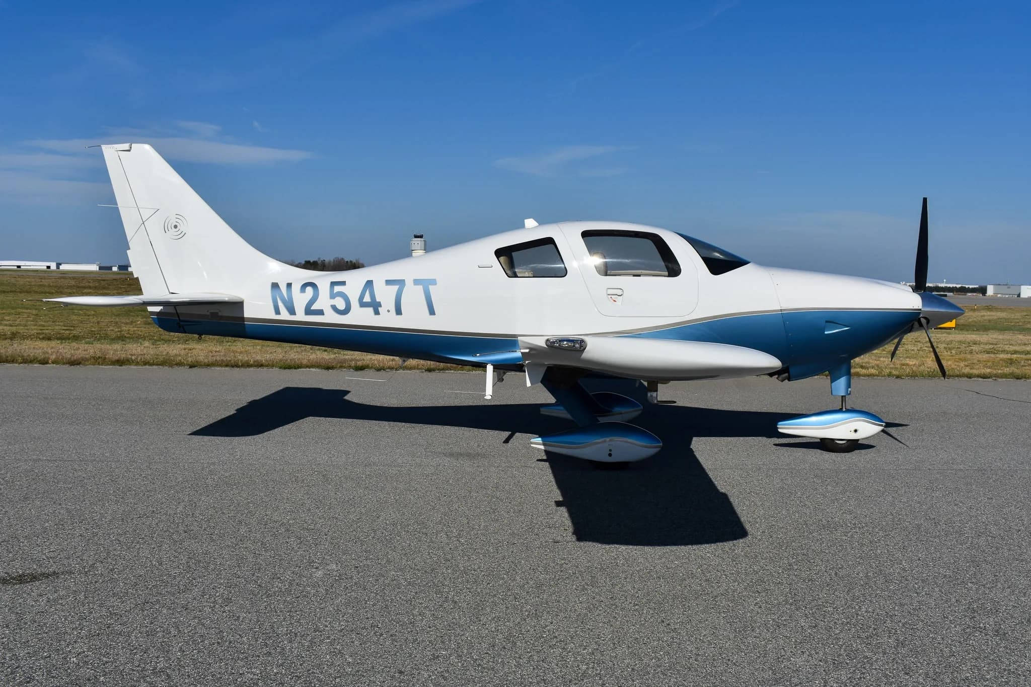 A white and blue single-engine aircraft, N2547T, parked on an asphalt runway under a clear blue sky.