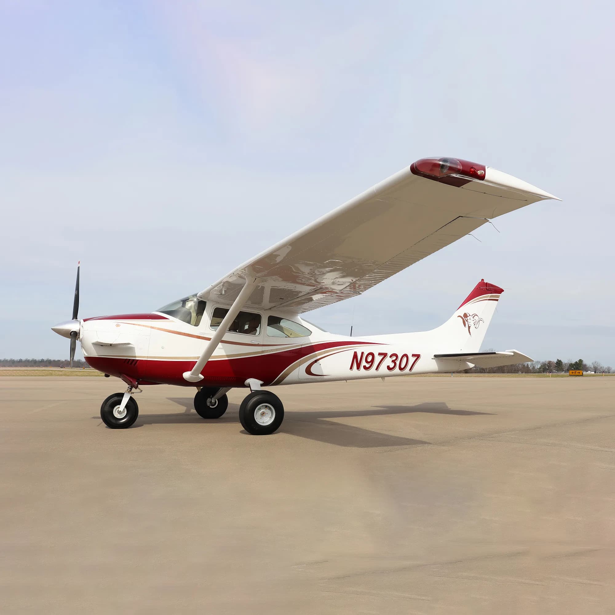 A white and red single-engine high-wing aircraft, N97307, parked on an airfield under a partly cloudy sky.