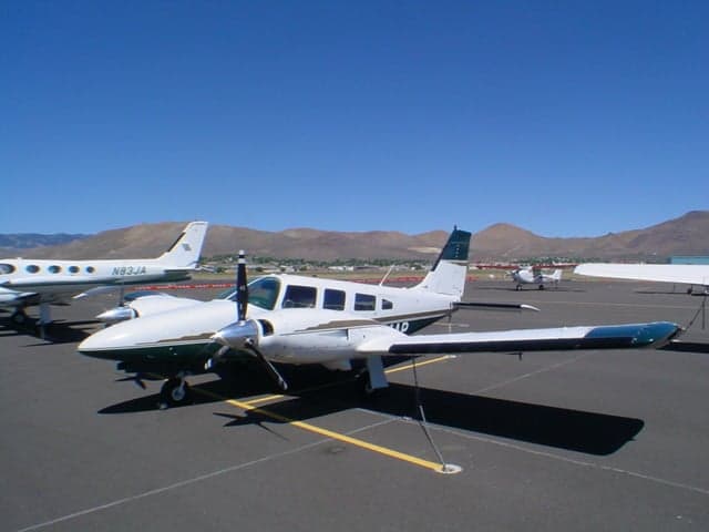 A white and dark green twin-engine Piper Navajo Chieftain (N634AP) is parked on an airport tarmac with mountains in the background.