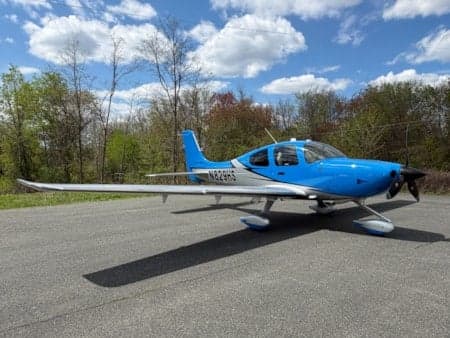 A blue and silver Cirrus SR22 aircraft, registration N829HS, parked on an asphalt surface under a partly cloudy sky.