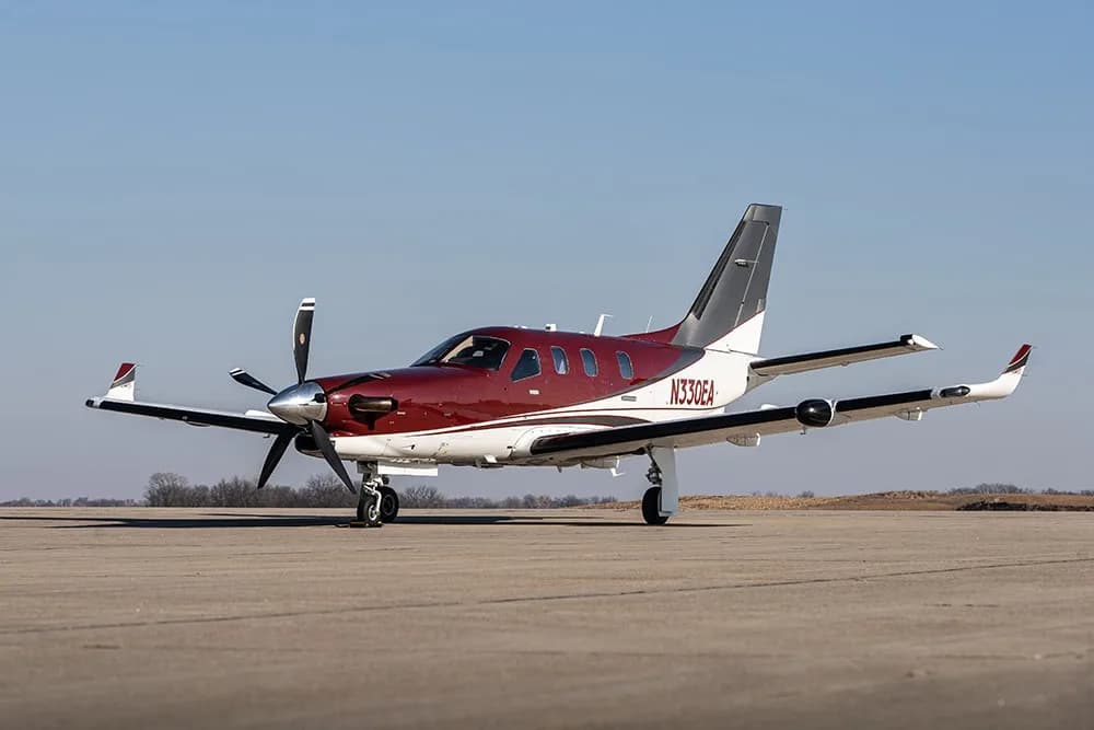 A maroon and white Daher TBM 900 turboprop aircraft with registration N330EA parked on an airfield.