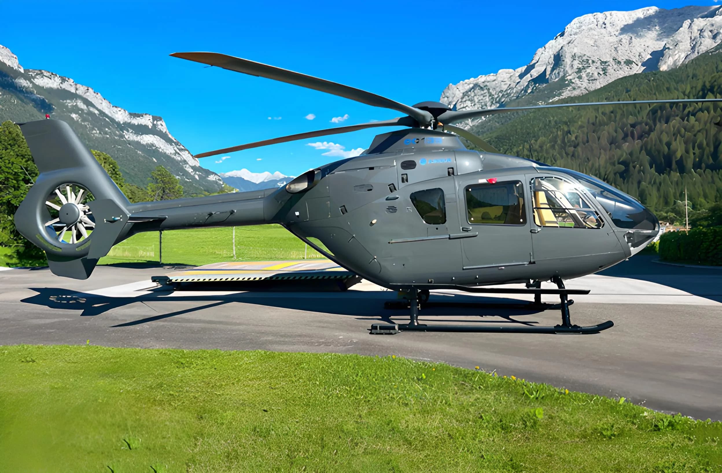 An Airbus helicopter is parked on the tarmac with mountains in the background.