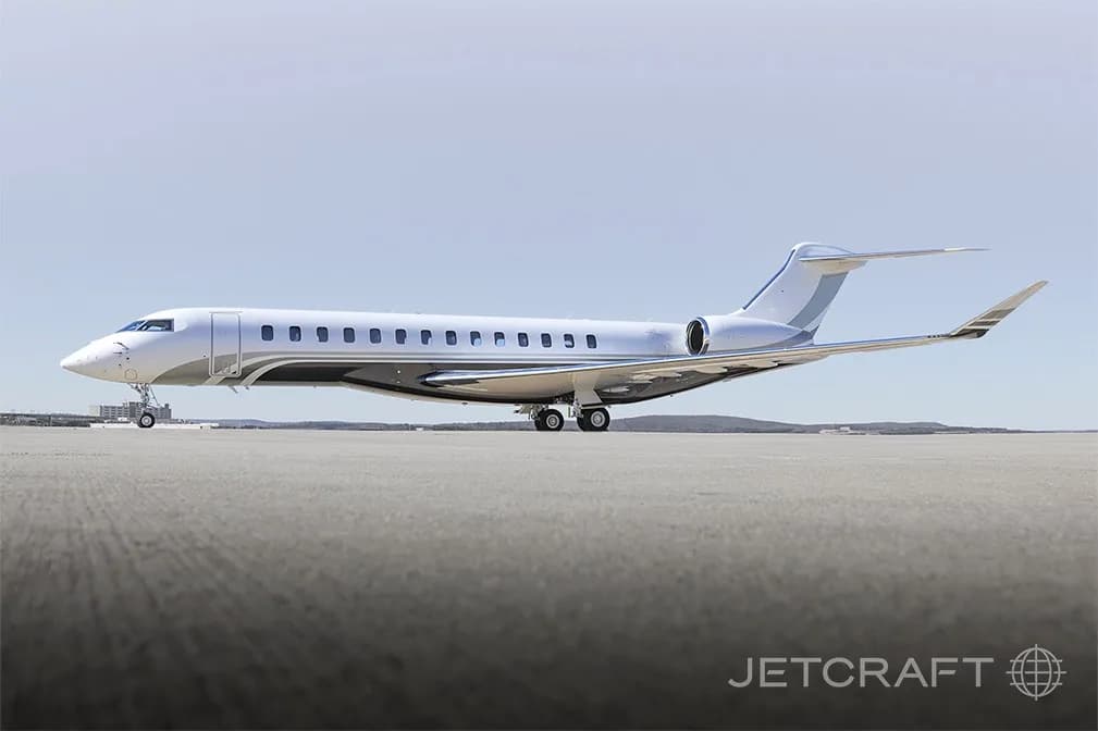 A white and grey Bombardier Global 7500 business jet parked on a tarmac under a clear sky.