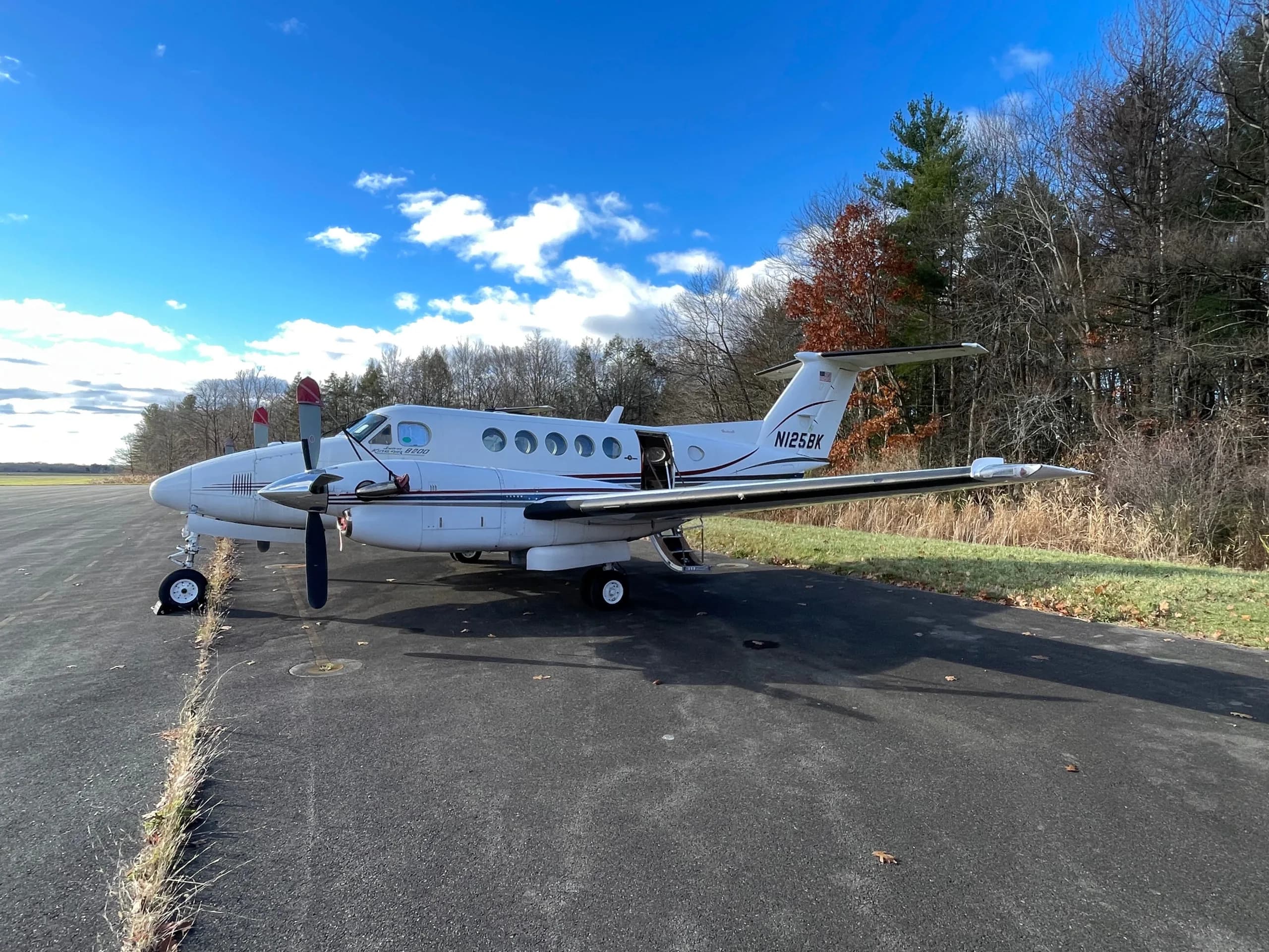 A white Beechcraft King Air 350 turboprop aircraft with red accents parked on an asphalt runway under a blue sky.