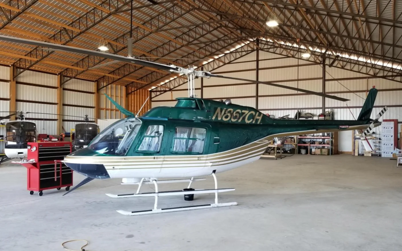A green and white helicopter with registration N867CH parked inside a hangar.