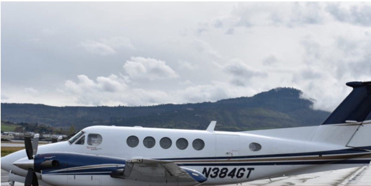A King Air aircraft with registration N384GT is parked on the tarmac with mountains in the background.