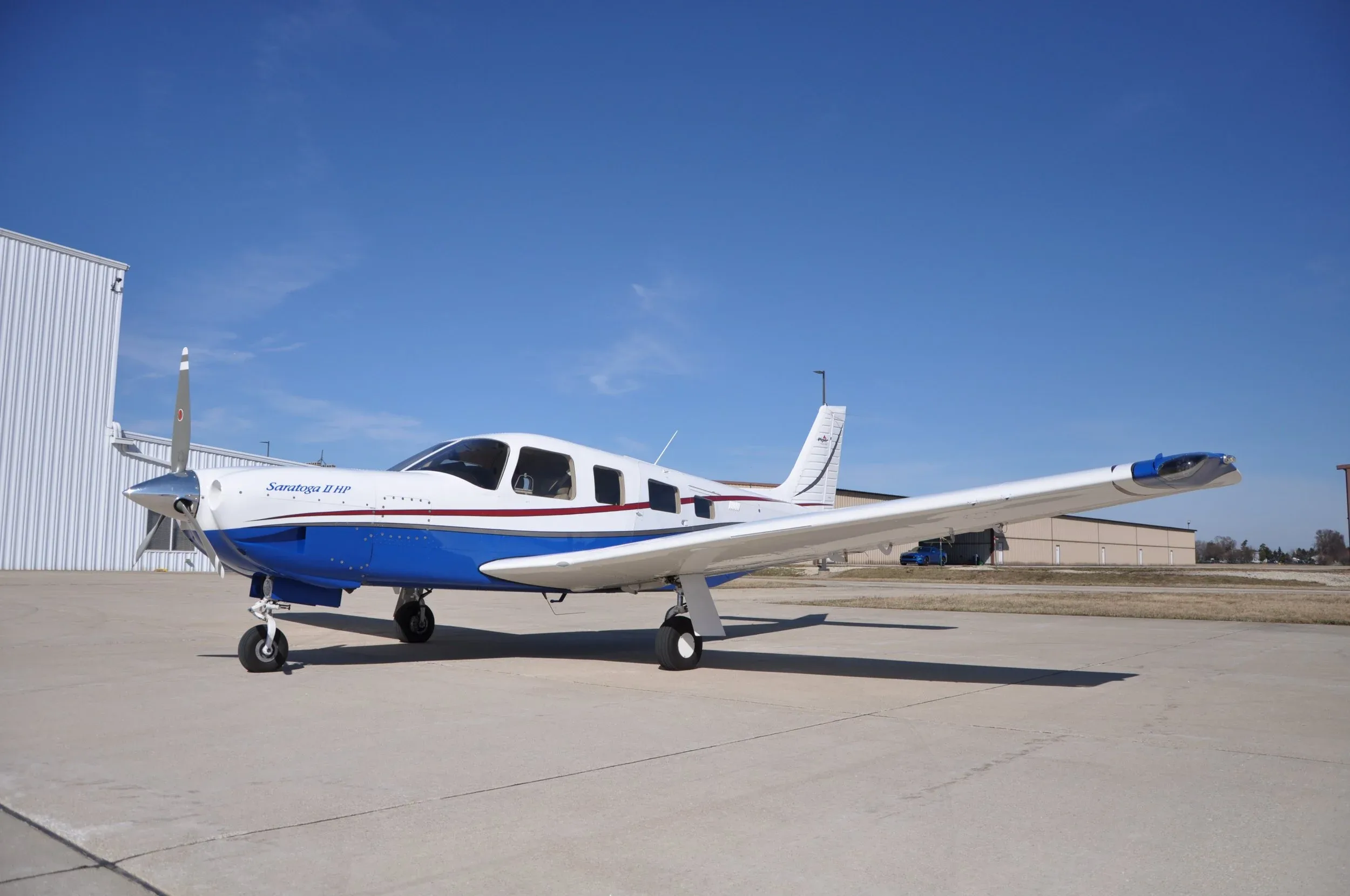 A Saratoga II HP aircraft is parked on the tarmac with a blue and white paint scheme.