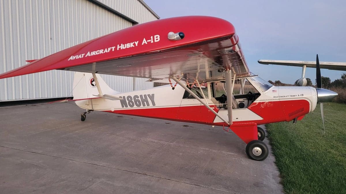 Aviat Aircraft Husky A-1B aircraft with a red and white paint scheme parked on the tarmac.