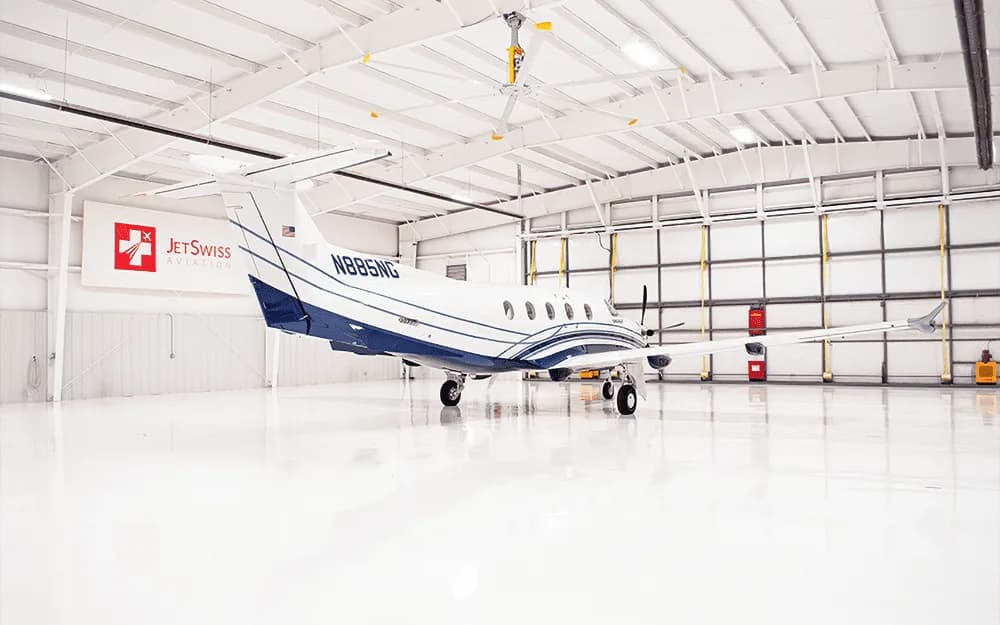 A white and blue Pilatus PC-12 aircraft, tail number N885NG, is parked in a brightly lit hangar.