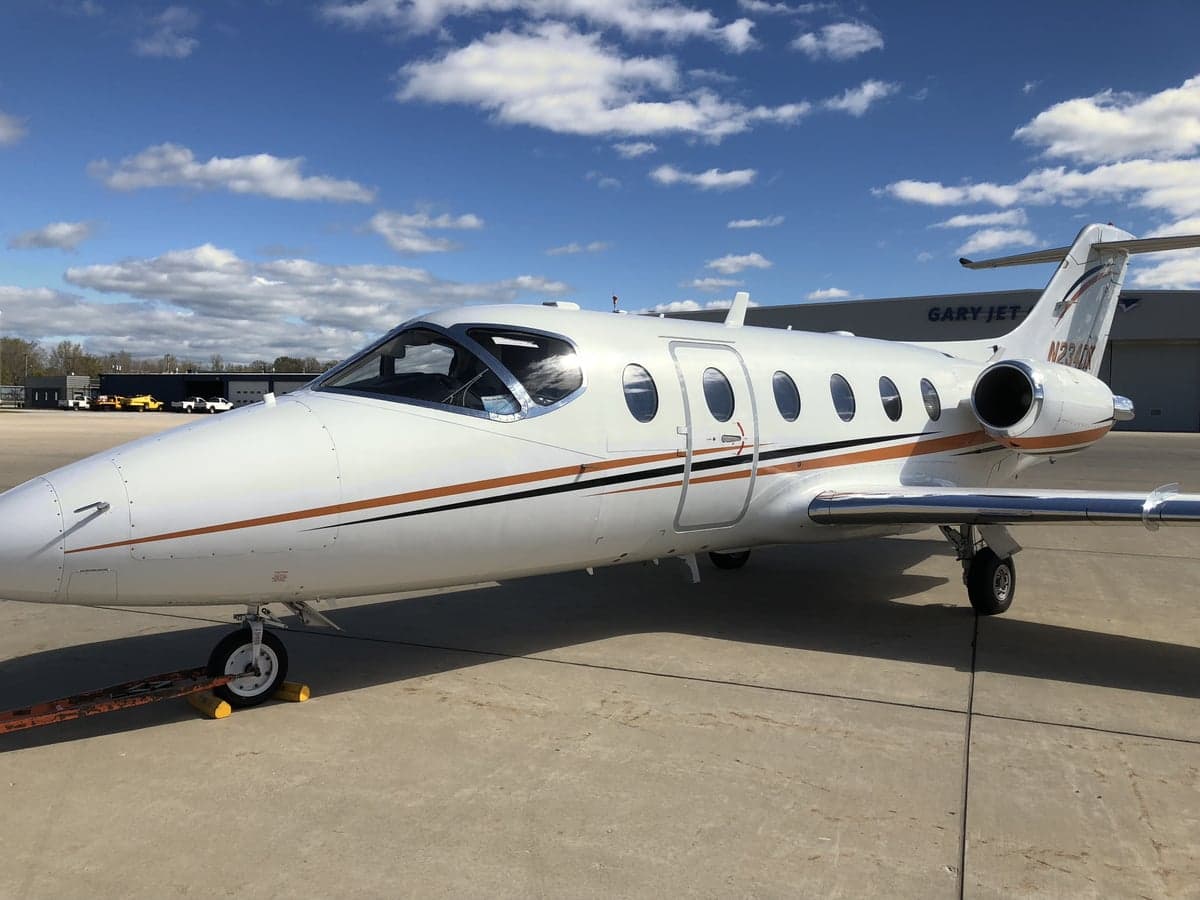 Side view of a white Hawker jet with orange and black stripes on the tarmac.