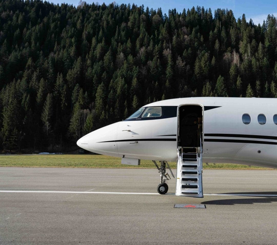 A white aircraft parked on the tarmac with the door open.
