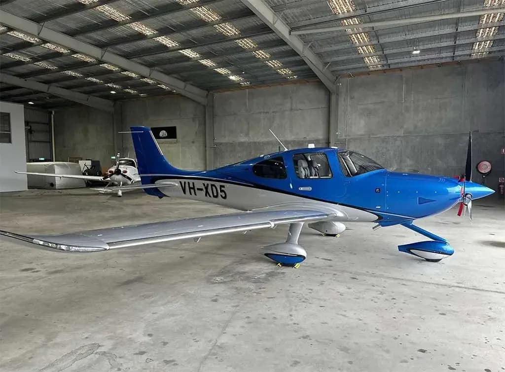 A blue and white Cirrus SR22 aircraft with registration VH-XD5 parked inside a large hangar.