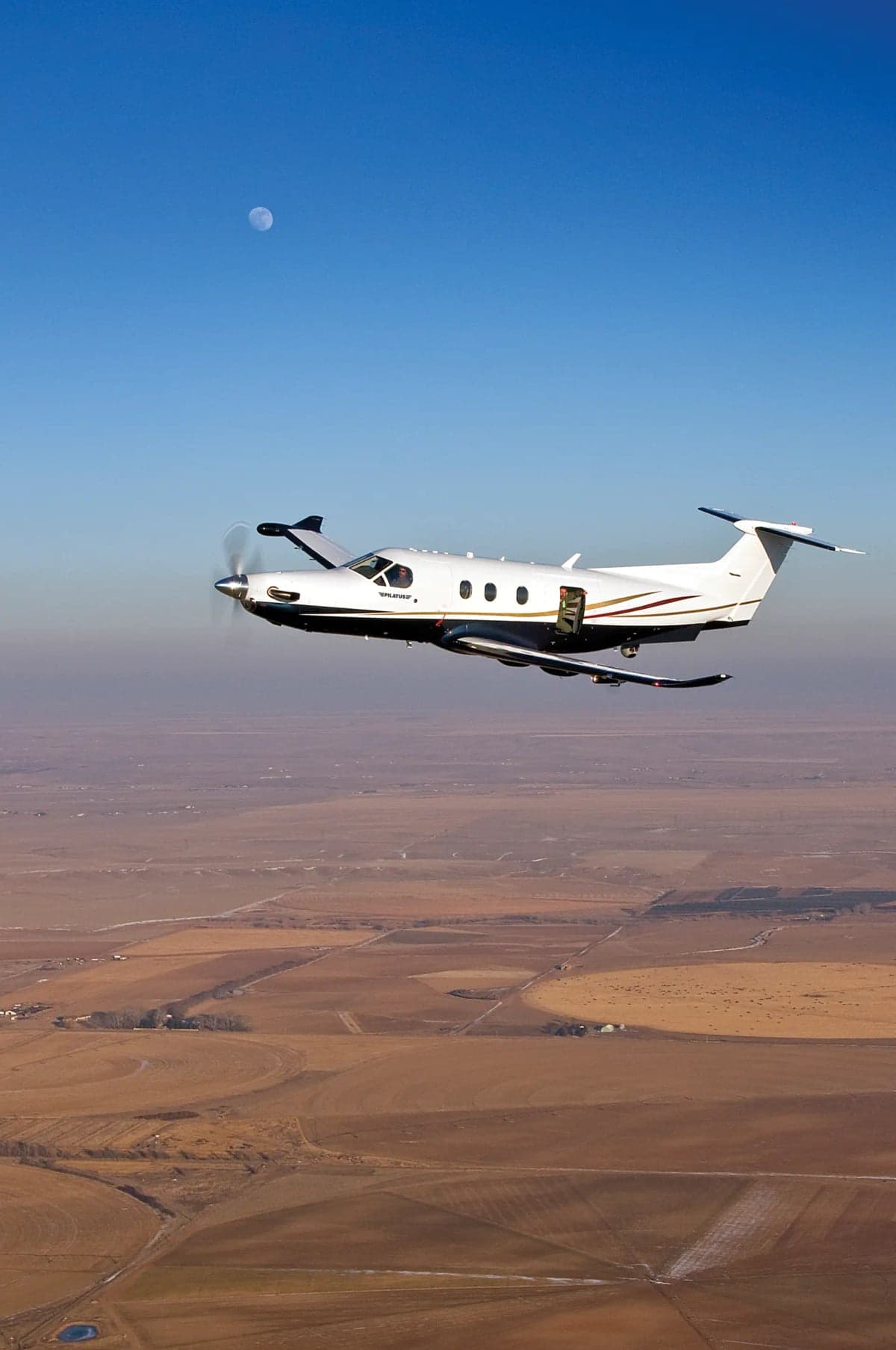 A Pilatus PC-12 aircraft in flight over a rural landscape.