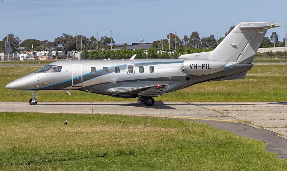 Side view of a silver and blue Embraer Phenom 300 with registration VH-PIL on the tarmac.