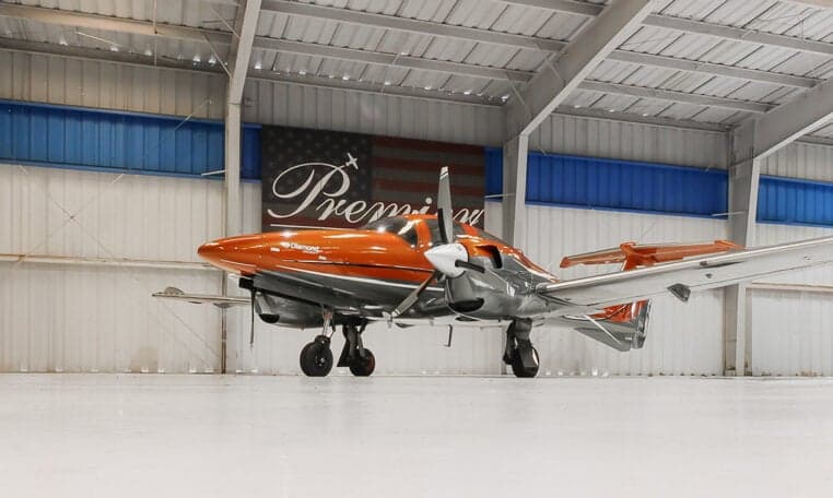 A Diamond DA62 aircraft with an orange and gray paint scheme is parked in a hangar.