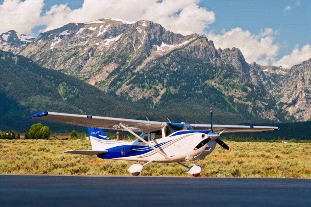 A Cessna Skylane parked on the tarmac with mountains in the background.