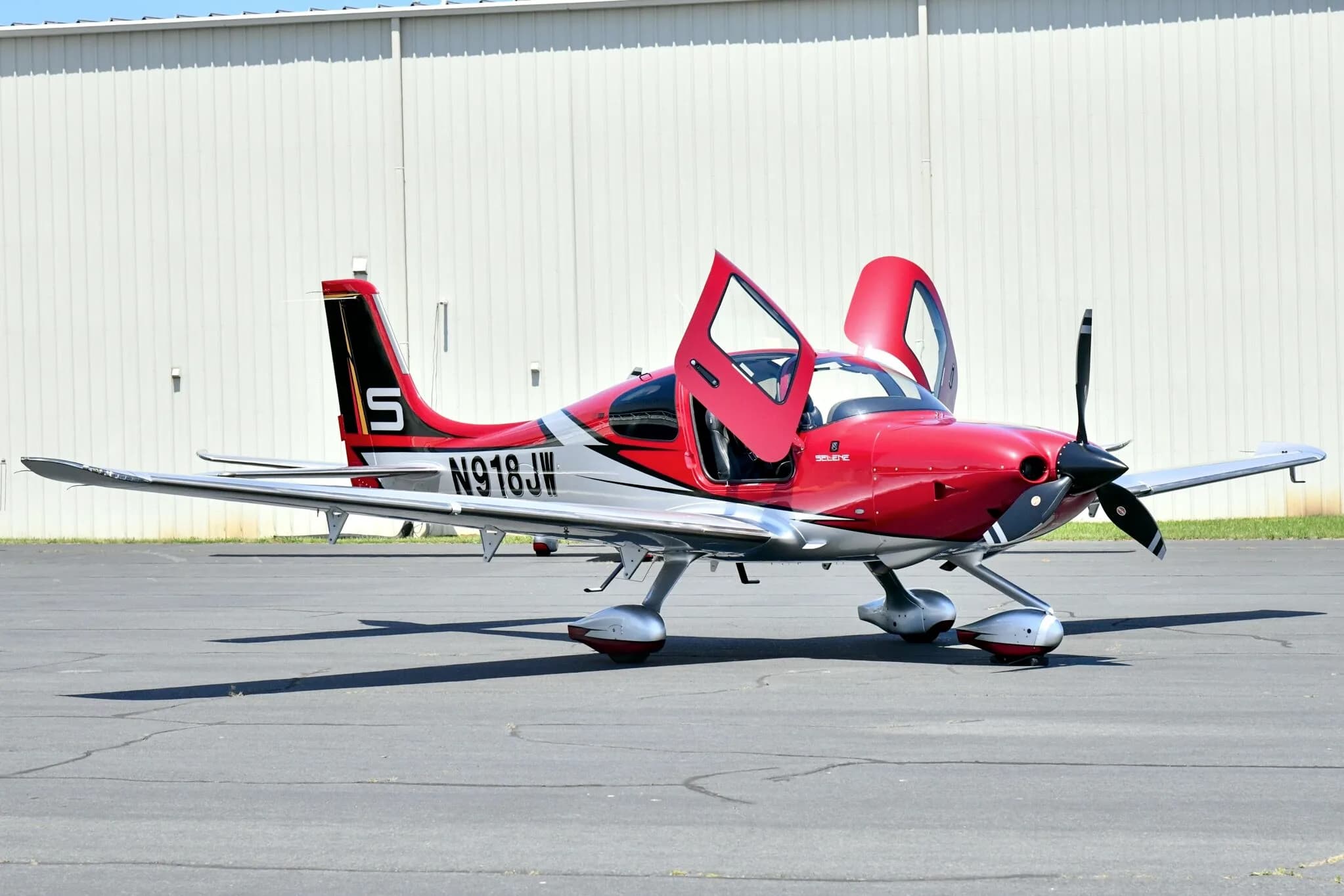 A red and white Cirrus SR22T aircraft with registration N918JW parked on an airfield with its doors open.