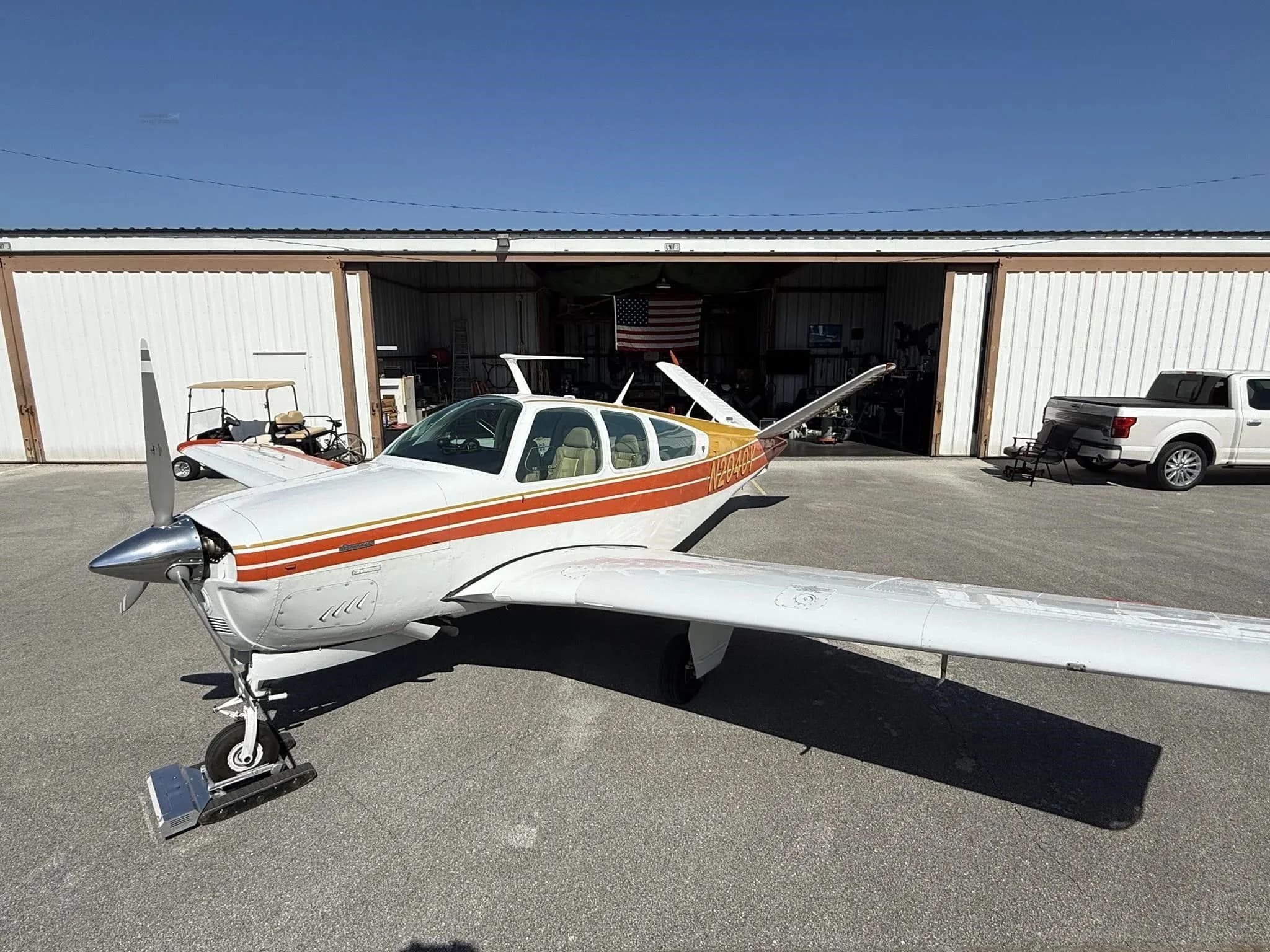 A white and orange single-engine aircraft, N2040Y, parked on an asphalt ramp in front of a hangar.