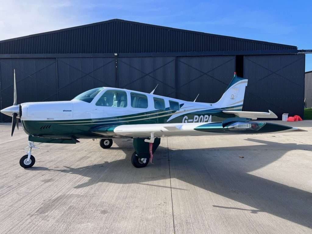 A Beechcraft Bonanza with a white and green paint scheme is parked on the tarmac.