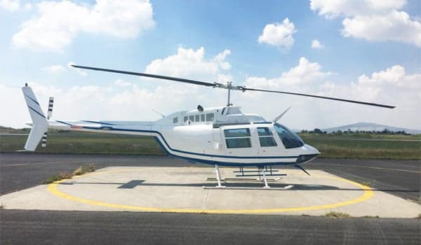 A white Bell 206 helicopter with blue accents is parked on a helipad.