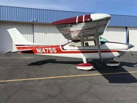 A red and white Cessna 172 aircraft, registration N1475S, is parked on an asphalt tarmac in front of a hangar.