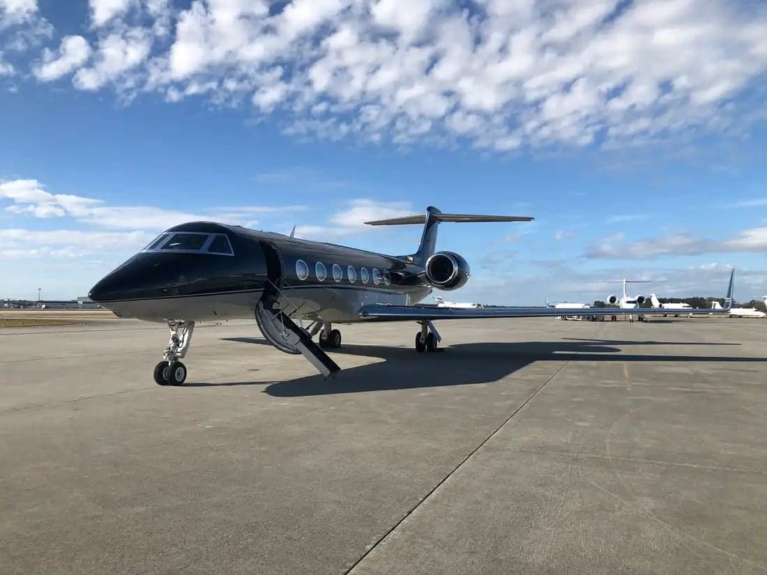 A black and silver Gulfstream business jet is parked on the tarmac with its door open.