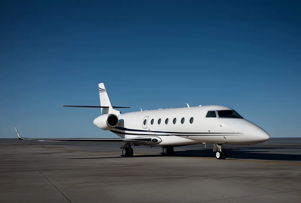 A white private jet with dark blue stripes on the tarmac under a clear blue sky.