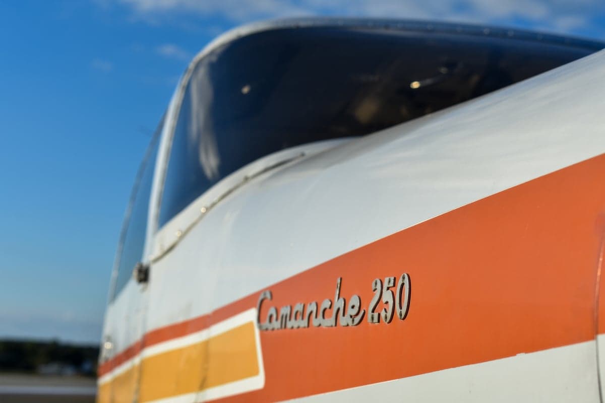 Piper Comanche 250 aircraft, front view, with white and orange paint scheme.