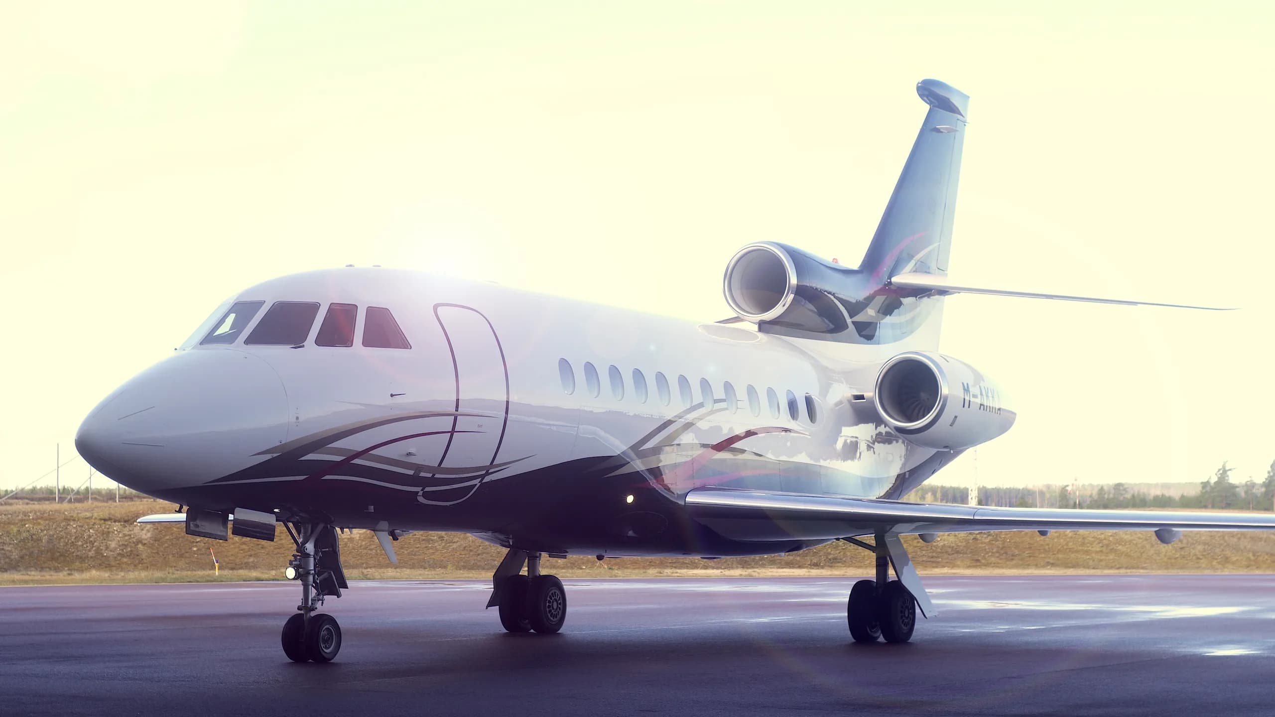 A Dassault Falcon 900 business jet with a white and dark blue paint scheme on a tarmac at sunset.
